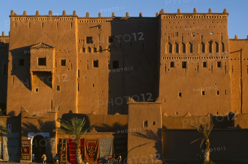 MOROCCO, Ouarzazate, View of red stone kasbah exterior with carpets hanging from the lower walls.