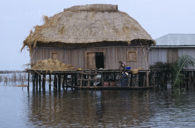 Benin, Ganvie, Thatched house on stilts in West African lake town, woman and children on a boat beside it.