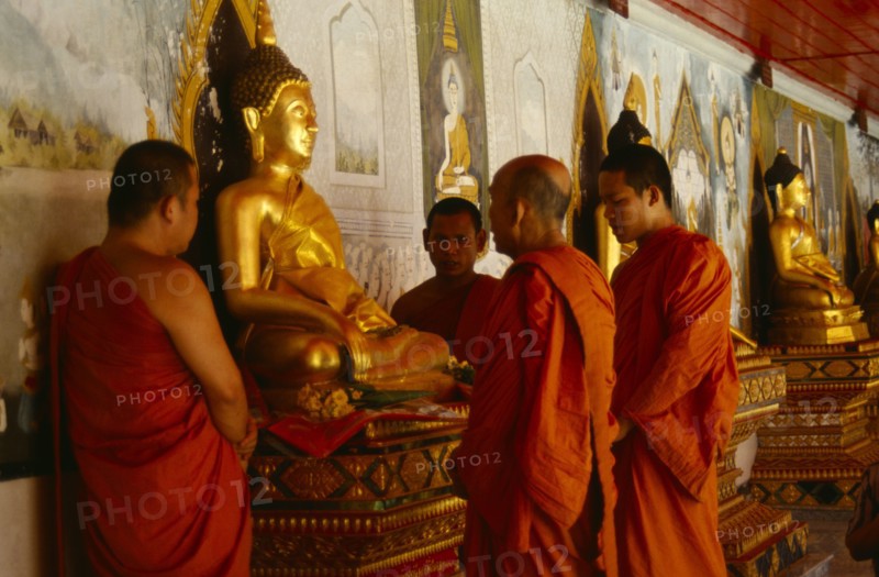 Thailand, Chiang Mai, Buddhist monks at Wat Doi Suthep praying on behalf of a family beside seated golden Buddha figure.