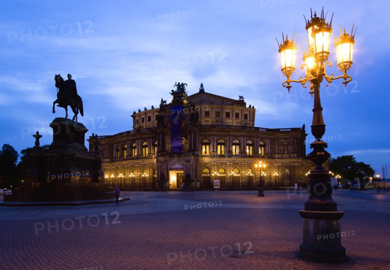 GERMANY, Saxony, Dresden, The restored Baroque Sachsische Staatsoper or State Opera House in Theatre Square first built in 1841 by architect Gottfried Semper illuminated at sunset with an equestrian statue of King Johann and an ornate lamppost in the foreground.