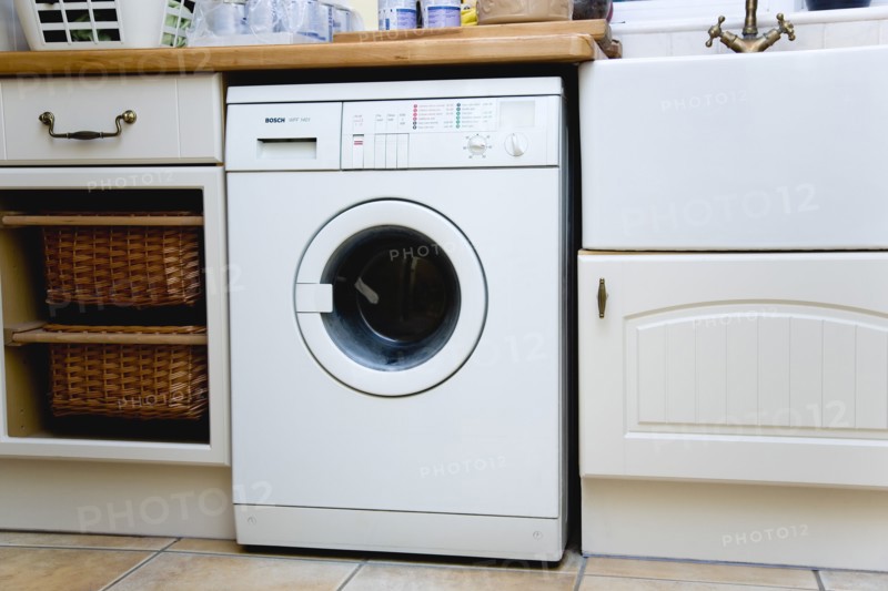 Architecture, Interiors, Machinery, White domestic washing machine household appliance set under worktop in utility laundry room.