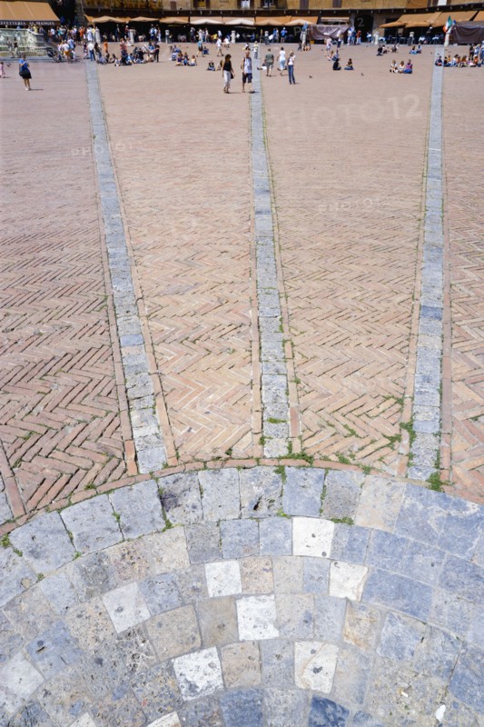 ITALY, Tuscany, Siena, The Piazza del Campo and surrounding buildings with tourists walking in the square. Three lines in flat stone laid into the herringbone brick pattern of the square radiate from the central drain towards the buildings.