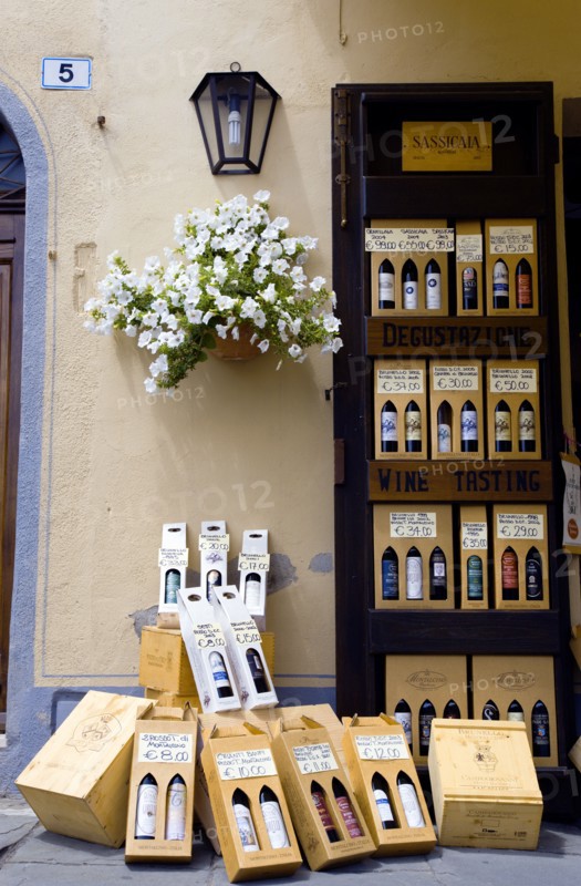 ITALY, Tuscany, Montalcino, Val D'Orcia Brunello di Montalcino Enoteca or wine shop with dispaly of boxed wines on the pavement by its entrance undera potted white gerranium plant beside a wine tasting sign.