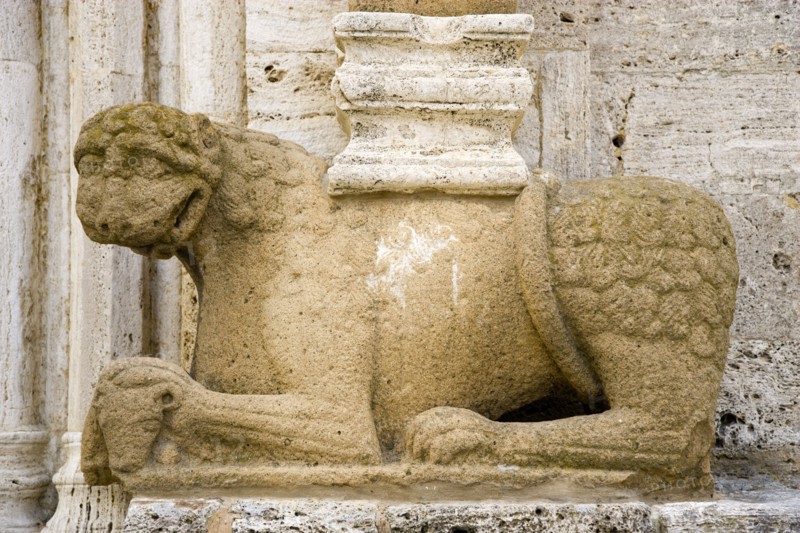 ITALY, Tuscany, San Quirico D'Orcia, The Collegiata Church of the saints Quirico and Giulitta. Sandstone carving of a lion, ossibly Etruscan, at the base of a caryatid or zoomorphic column at the entrance to the church.