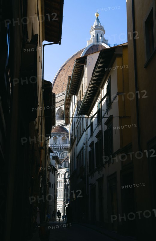 ITALY, Tuscany, Florence, The Dome of the Cathedral of Santa Maria del Fiore the Duomo by Brunelleschi and marble sides of the church seen down a narrow street with people walking past.