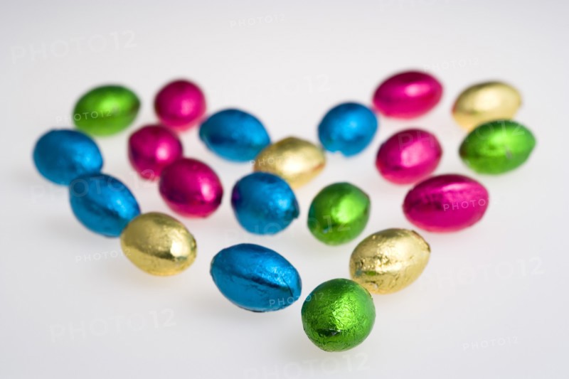 Food, Sweets, Chocolate, Colourful foil wrapped Easter eggs in the shape of a Valentine heart on a white background.
