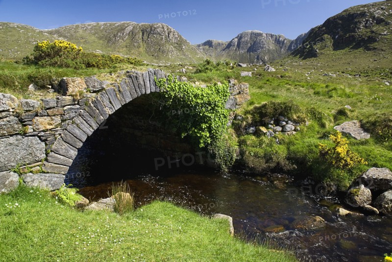 IRELAND, County Donegal, The Poisoned Glen, A stream runs under an old style stone bridge with the Derryveagh Mountain behind.