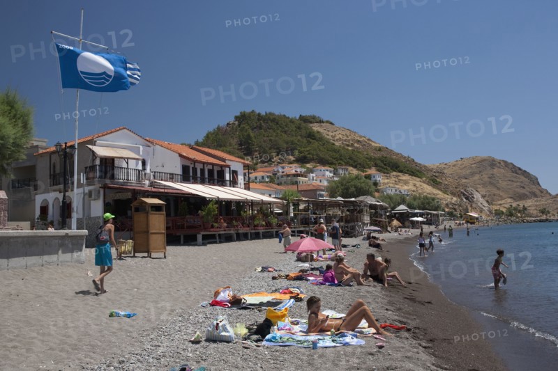 GREECE, North East Aegean, Lesvos Island, Eresos, View of beach with people sunbathing and swimming just in front of the villages bars and restaurants.