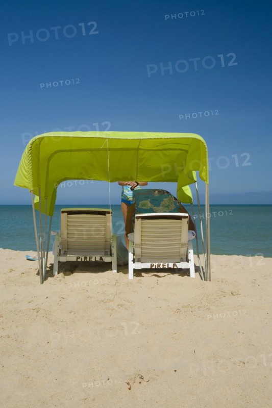 VENEZUELA, Margarita Island, Playa Caribe, View of a green tent at the Playa Caribe beach with a person reading the Margarita Islands map under the shade of the tent, just in front of the exotic seawater, shoot on a bright day with blue sky.