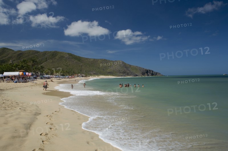 VENEZUELA, Margarita Island, Playa Caribe, View of exotic beach with people swimming and walking on the sand while deck chairs, bars and restaurants are noticeable, shoot on a bright day with blue sky and white clouds.