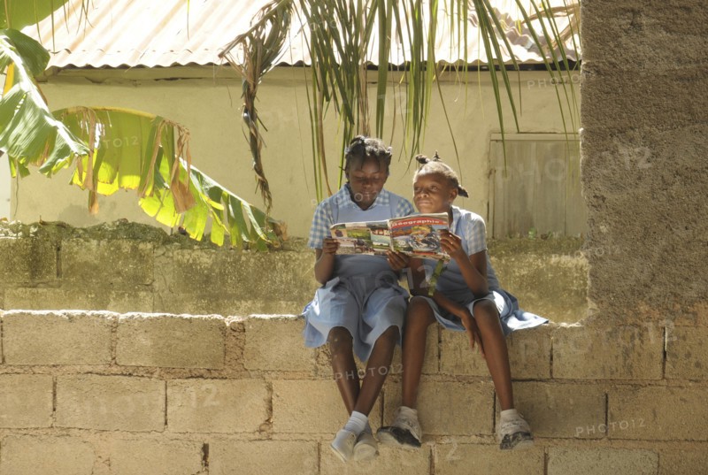 HAITI, Isla de la Laganave, young school girls sat on wall reading geography magazine.