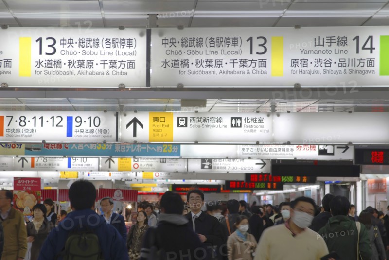 Japan, Tokyo, Shinjuku, inside JR Shinjuku train station, crowd of passengers walking under jumble of train signs, bilingual signs.