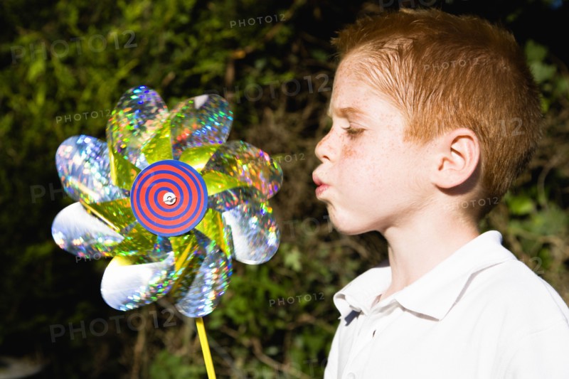 Children, Toys, Outdoors, Young red haired boy blowing toy windmill gently.