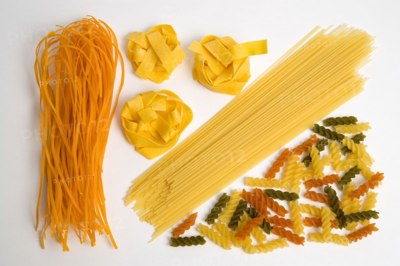Food, Uncooked, Pasta, Varieties of orange flavoured Taglioline yellow Pappardelle Spaghetti and three colour tricolore Fusilli arranged on a white background.
