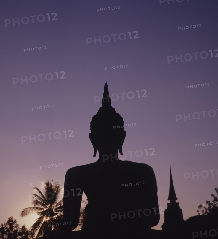 Thailand, Sukhothai, Wat Mahathat, Seated Buddha Statue silhouetted against purple coloured evening sky.