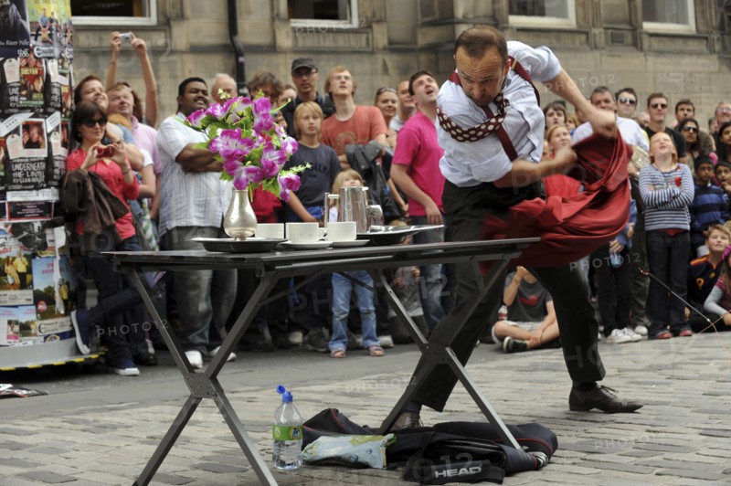 Scotland, Lothian, Edinburgh Fringe Festival of the Arts 2010, Street performers and crowds on the Royal Mile, magaician pulling table cloth from under plates.