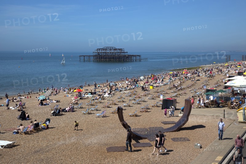 England, East Sussex, Brighton, view over the pebble beach with modern sculpture in the foreground and the burnt out ruins of the West Pier in the background.