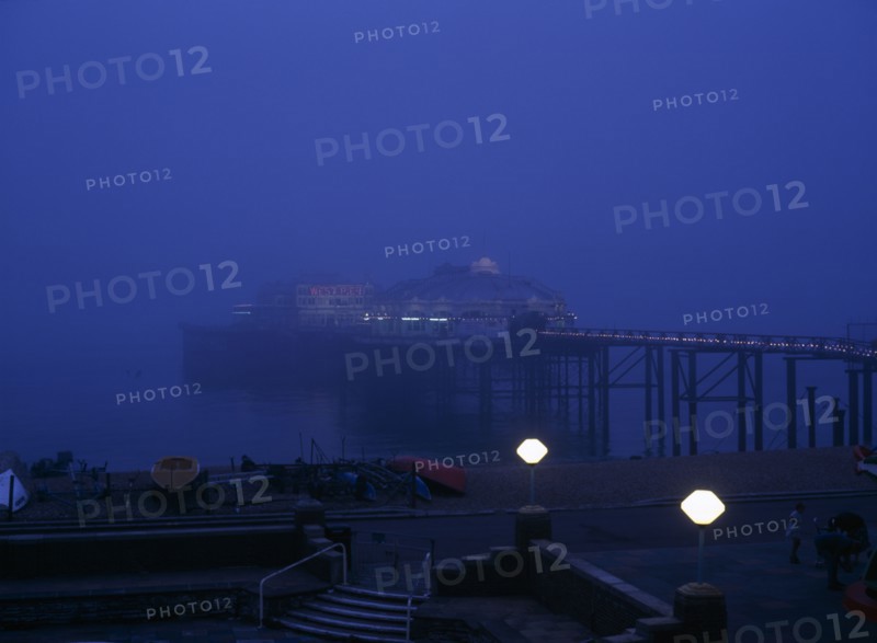 Brighton, East Sussex, England. The West Pier illuminated in evening light with mist on the sea European Great Britain Northern Europe UK United Kingdom Warm Light Water