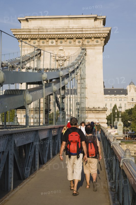 Budapest, Pest County, Hungary. Tourists with matching day packs crossing Szechenyi Chain Bridge or Memory Bridge over the River Danube on foot. Hungary Hungarian Europe European East Eastern Buda Pest Budapest City Architecture Bridge Transport Szechenyi Chain Memory Walking people Pedestrians Tourists Destination Destinations Eastern Europe Holidaymakers Tourism