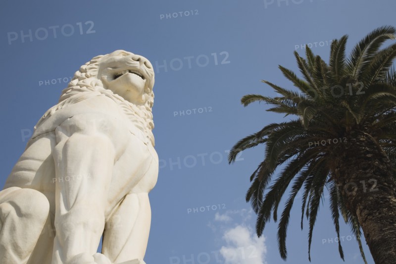 Samos Island, Northern Aegean, Greece. Vathy. Lion statue in Pythagoras Square set up in 1930 to mark the centenary of the uprising against the Ottoman Turkish overlords. Greece Greek Europe European Vacation Holiday Holidays Travel Destination Tourism Ellas Hellenic Northern Aegean Samos Vathy Lion Statue Art Carved Pythagoras Square Architecture Blue Sky Palm Tree Destination Destinations Ellada History Historic Southern Europe