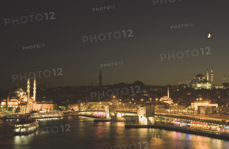 Istanbul, Turkey. Sultanahmet. The Golden Horn. The New Mosque or Yeni Camii at left the Galata Bridge and Suleymaniye Mosque at right illuminated at night with crescent moon in sky above. Turkey Turkish Istanbul Constantinople Stamboul Stambul City Europe European Asia Asian East West Urban Skyline Destination Travel Tourism Sultanahmet Golden Horn New Mosque Yeni Camii Galata Bridge Suleymaniye Dusk Sunset Night Illuminated Skyline Minarets Water Crescent Moon Blue Citiscape Building Buildings Urban Architecture Destination Destinations Middle East Nightfall Twilight Evenfall Crespuscle Crespuscule Gloam Gloaming Nite South Eastern Europe Sundown Atmospheric Turkiye Western Asia