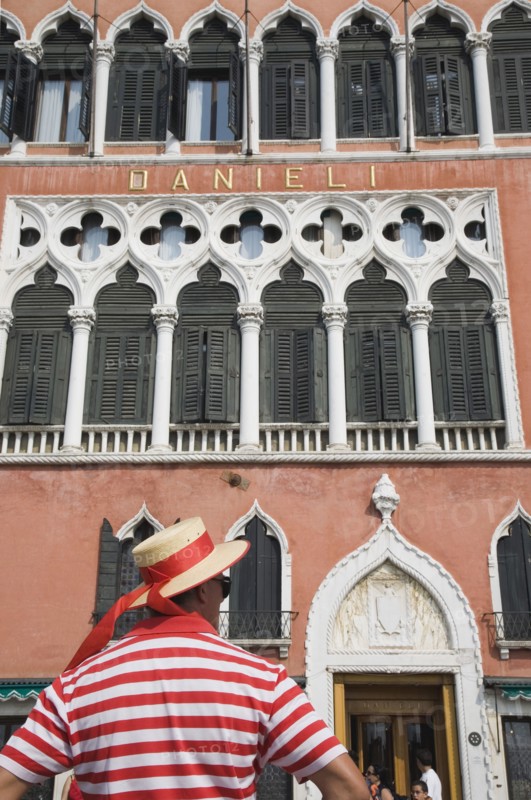 Venice, Veneto, Italy. Cropped shot of gondolier wearing red and white striped shirt and straw boater trimmed with red sash standing in front of facade of the Hotel Danieli. Italy Italia Italian Venice Veneto Venezia Europe European City Red Gondolier Man Striped Stripe Stripes Architecture Facade Hotel Danieli Hat Sash Ribbon Band Window Windows Shutters Color Destination Destinations Male Men Guy One individual Solo Lone Solitary Southern Europe