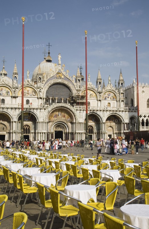 Venice, Veneto, Italy. Centro Storico St. Marks Square Cafe tables prepared for customers in early morning sunshine with facade of Basilica di San Marco behind. Italy Italia Italian Venice Veneto Venezia Europe European City Centro Storico St saint Mark Marks Square Cafe Cafes Restaurants Tables Chairs Yellow White Basilico San Marco Bar Bistro Blue Destination Destinations Religion Religious Southern Europe