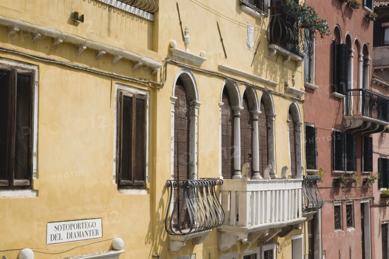 Venice, Veneto, Italy. Restored facades of canalside buildings painted pastel pink terracotta and yellow with window balconies and shutters in late summer sunshine. Italy Italia Italian Venice Veneto Venezia Europe European City Architecture Canal Yellow Balconies Exterior Facade Color Destination Destinations Southern Europe