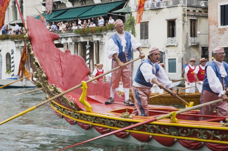 Venice, Veneto, Italy. Participants in the Regatta Storico historical annual regatta wearing traditional costume rowing gondola past onlookers gathered on the balconies of canalside buildings behind. Italy Italia Italian Venice Veneto Venezia Europe European City Regata Regatta Gondola Gondola Gondolas Gondolier Boat Architecture Exterior Water Classic Classical Destination Destinations History Historic Holidaymakers Older Southern Europe Tourism Tourist