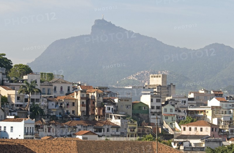Rio de Janeiro, Brazil. Rooftops of Saude neighbourhood with a hillside favela or slum and the statue of Christ the Redeemer atop Corcovada mountain traditional tile roofs and palm trees. Brazil Brasil Brazilian Brasilian South America Latin Latino American City Urban Architecture Houses Housing Homes Favela Slum Corcovado Christ Statue Redeemer Saude Classic Classical Destination Destinations Historical Latin America Older Shanty South America Southern