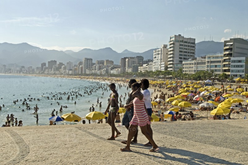 Rio de Janeiro, Brazil. Crowds at Ipanema beach with yellow umbrellas blue sea and sky swimmers in sea and hotels along the Avenue Vieira Souto with group of young women in foreground. Brazil Brasil Brazilian Brasilian South America Latin Latino American City Travel Destination Urban Vacation Beach Beaches People Sunbathing Crowds Childre Kids Young Ipanema Swimmers Swimming Hotels Sea Avenue Viera Souto Destination Destinations Female Woman Girl Lady Holidaymakers Immature Latin America Sand Sandy Beach Tourism Seaside Shore Tourist Tourists Vacation Sand Sandy Beaches Tourism Seaside Shore Tourist Tourists Vacation South America Southern Sunbather Water