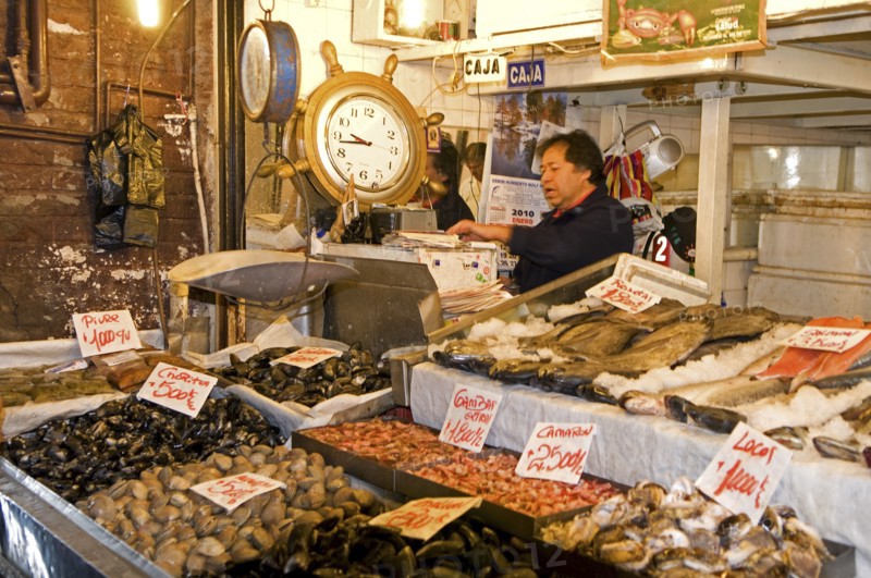 Santiago, Chile. Mecardo Central. Shellfish fresh fish and octopus on sale with prices clearly displayed. Vendor behind counter by a large clock and weighing scale. With a 5 million ton annual catch the country is the seventh-largest fishing nation in the world. Chile Chilean South America American Hispanic Santiago City Cityscape Urban Travel Destination Vacation Holiday Mercado Central Market Fish Seafood Shellfish Scales Clock Destination Destinations Five Latin America Latino One individual Solo Lone Solitary South America Southern