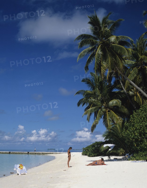 Beach, Maldives. Beach with tourists sunbathing next to the Indian Ocean. Maldives Island Islands Paradise Holiday Sea Water Travel Calm Blue Sky Beach Sand Shore Coast Indian Ocean Asia Asian Palm Trees Clear Vacation Tourists Color Destination Destinations Divehi Rajje Holidaymakers Sand Sandy Beaches Tourism Seaside Shore Tourist Tourists Vacation Sunbather