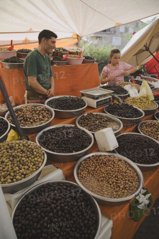 Kusadasi, Aydin Province, Turkey. Stall at weekly market selling olives and nuts with male stall holder and young girl standing behind display and set of electronic scales. Turkey Turkish Eurasia Eurasian Europe Asia Turkiye Aydin Province Kusadasi Market Markets Stall Display Olive Olives Dried Nut Nuts Scales Electronic Multi Muliple Color Colour Colors Colours Colored Coloured Destination Destinations European Immature Kids Middle East South Eastern Europe Western Asia