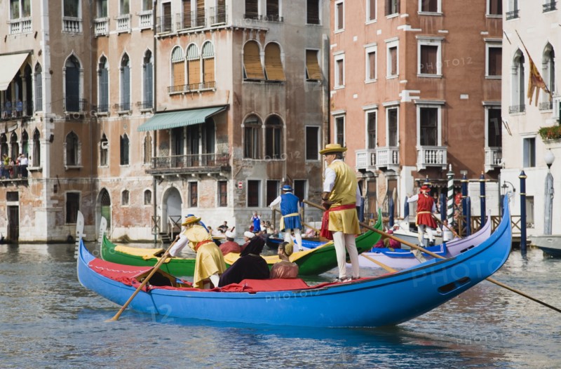 Venice, Veneto, Italy. Participants in the Regata Storico annual historical regatta in brightly painted gondolas and wearing traditional costume approaching the Rialto bridge with onlookers on balconies of canalside buildings behind. Teams represent Sestiere districts of Venice in traditional races. Italy Italia Italian Venice Veneto Venezia Europe European City Regata Regatta Gondola Gondola Gondolas Gondolier Boat Architecture Exterior Water Classic Classical Color Destination Destinations History Historic Older Southern Europe