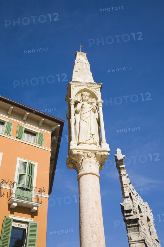 Verona, Veneto, Italy. Pastel painted facade of building with pale green painted window shutters and balconies with religious statue on free standing pillar in foreground against cloudless blue sky. Italy Italia Italian Veneto Verona Europe European City Sky Blue Christian Religion Religious Statue Shutters Shuttered Windows Window Exterior Exterior Facade Colourful Colorful Destination Destinations Religion Religious Christianity Christians Southern Europe