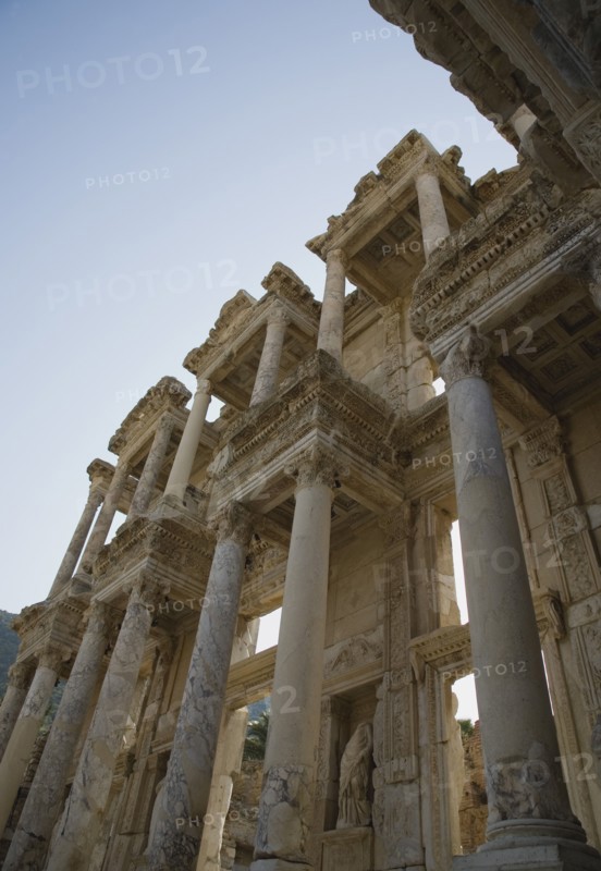 Selcuk, Izmir Province, Turkey. Ephesus. Roman Library of Celsus facade angled view looking upwards against clear pale blue sky. Turkey Turkish Eurasia Eurasian Europe Asia Turkiye Izmir Province Selcuk Ephesus Ruin Ruins Roman Library Celcus Column Columns Facde Ancient Architecture Masonry Rock Stone Destination Destinations European History Historic Middle East South Eastern Europe Western Asia