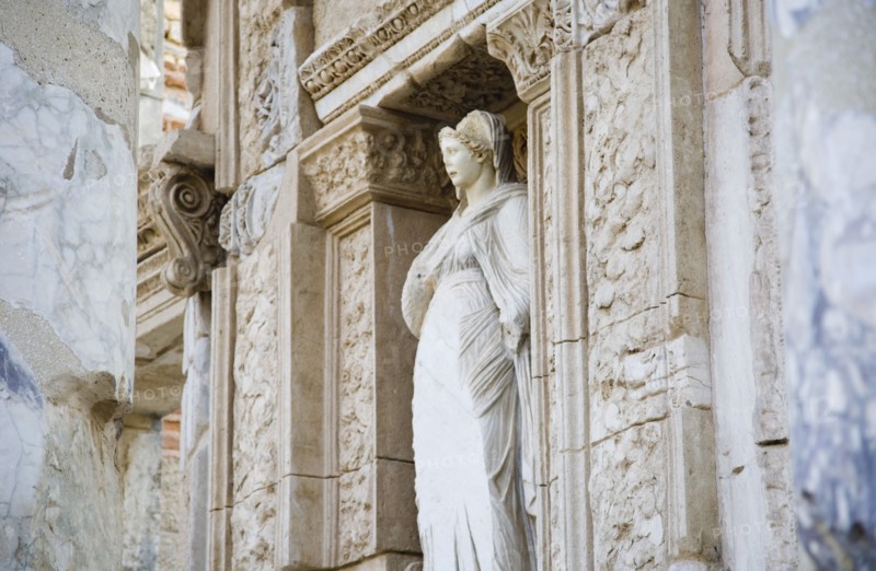 Selcuk, Izmir Province, Turkey. Ephesus. Damaged statue of female figure set in alcove of wall decorated with carvings in the antique city of Ephesus on the Aegean sea coast. Turkey Turkish Eurasia Eurasian Europe Asia Turkiye Izmir Province Selcuk Ephesus Ruin Ruins Roman Facde Ancient Architecture Masonry Rock Stone Statue Figure Destination Destinations European History Historic Middle East South Eastern Europe Water Western Asia