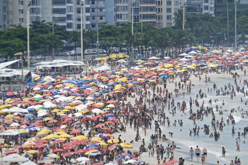 Rio de Janeiro, Brazil. Copacabana beach. Crowds on the beach and in the sea and multi-coloured beach umbrellas with part seen apartment buildings behind. Brazil Brasil Brazilian Brasilian South America Latin Latino American City Travel Destination Urban Vacation Beach Beaches People Sunbathing Crowds Rio de Janeiro Copacabana Umbrellas Parasols Destination Destinations Flat Holidaymakers Latin America Sand Sandy Beach Tourism Seaside Shore Tourist Tourists Vacation Sand Sandy Beaches Tourism Seaside Shore Tourist Tourists Vacation South America Southern Sunbather Water