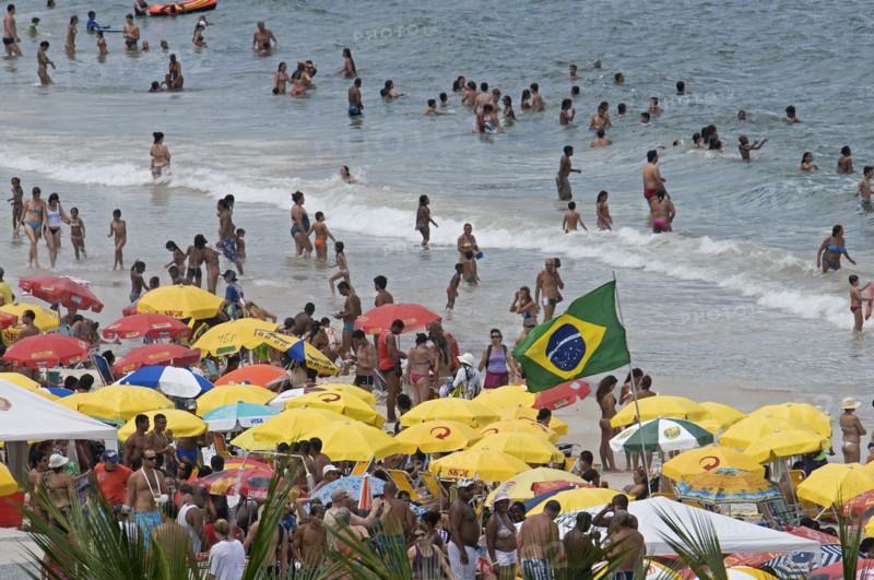Rio de Janeiro, Brazil. Copacabana beach. Crowds on the beach and in the sea bikinis multi-coloured beach umbrellas and Brazilian flag. Brazil Brasil Brazilian Brasilian South America Latin Latino American City Travel Destination Urban Vacation Beach Beaches People Sunbathing Crowds Rio de Janeiro Copacabana Umbrellas Parasols Destination Destinations Holidaymakers Latin America Sand Sandy Beach Tourism Seaside Shore Tourist Tourists Vacation Sand Sandy Beaches Tourism Seaside Shore Tourist Tourists Vacation South America Southern Sunbather Water