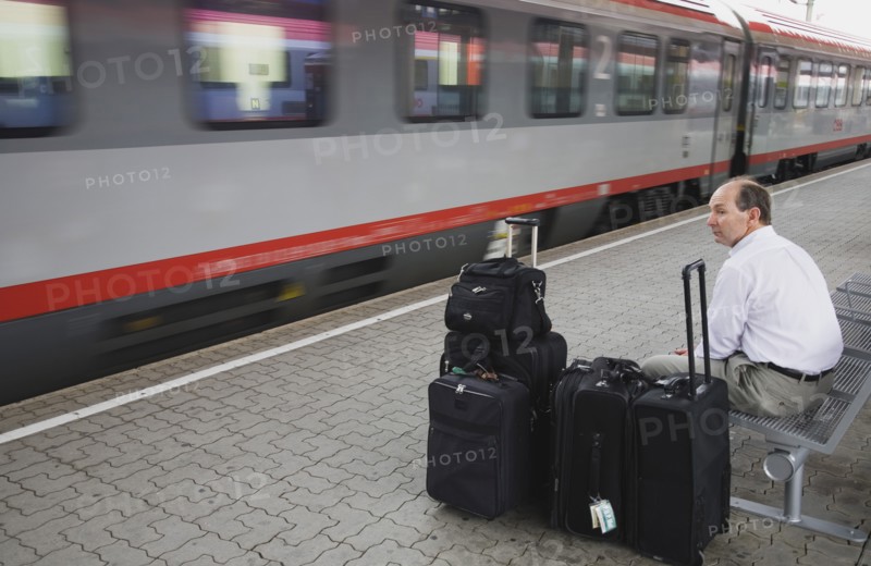 Vienna, Austria. Wien Westbahnhof. Passenger with luggage sitting on Vienna West Station with passing train. Also known as Vienna Western Station this is a major Austrian station and the starting point of the Austrian Western Railway or Westbahn for trains to Salzburg Munich Frankfurt Zurich Budapest Bucharest Belgrad etc. Austria Austrian Republic Vienna Viennese Wien Europe European City Capital Westbahnhof Transport Rail Train Train Station Commuter Tourist Luggage Baggage Bags man Destination Destinations Male Men Guy MŸnchen One individual Solo Lone Solitary Osterreich Sightseeing Tourists Viena Western Europe