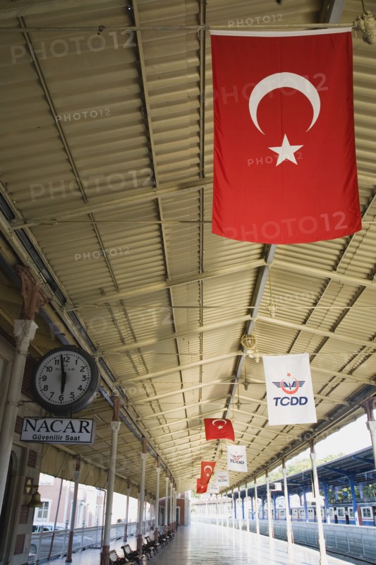 Istanbul, Turkey. Sultanahmet. View along railway platform with Turkish flags hanging from the roof. Istanbul Sirkeci Terminal or Sirkeci GarA is a terminus main station of the Turkish State Railways or TCDD in Sirkeci on the European part of Istanbul. International domestic and regional trains running westwards depart from this station which was inaugurated as the terminus of the Orient Express. Turkey Turkish Istanbul Constantinople Stamboul Stambul City Europe European Asia Asian East West Urban Destination Travel Tourism Transportt Rail Railway Train Trains Station Platform Clock Commuter Sirkeci TCCD Color Destination Destinations Middle East South Eastern Europe Turkiye Western Asia