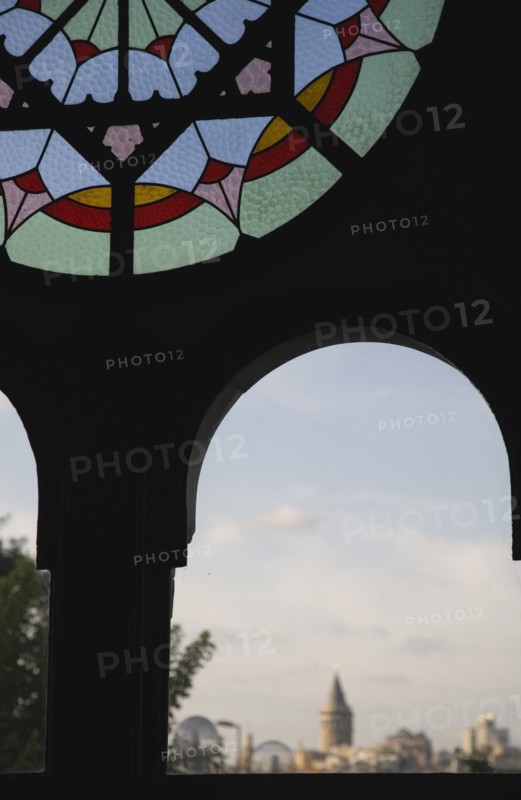 Istanbul, Turkey. Sultanahmet. Part view of dirty stained glass window in Ottoman era waiting room framing view to Galata Tower on Golden Horn. Turkey Turkish Istanbul Constantinople Stamboul Stambul City Europe European Asia Asian East West Urban Destination Travel Tourism Sultanahmet Stainned Glass Window Windows Ottoman Dirty Destination Destinations Middle East South Eastern Europe Turkiye Western Asia