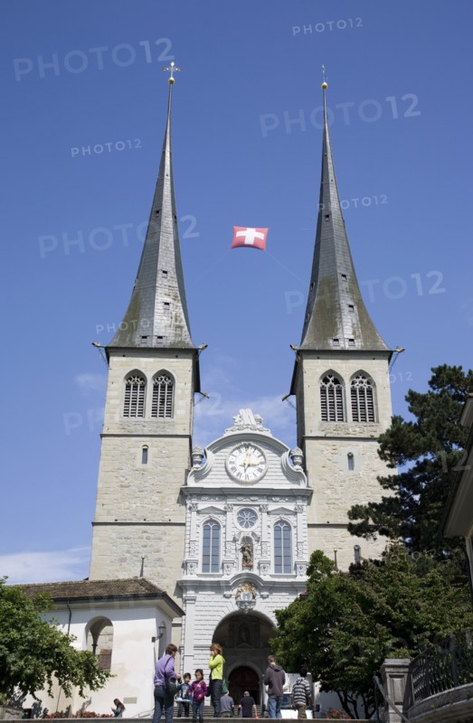 Lucerne, Switzerland. St Leodegar Church exterior with tourists. Switzerland Swiss Lucerne Lucerna Luzern St Saint Leodegar Church Exterior Facade Europe European Urban City Tourist Tourists Tourism Travel People Family Spire Spires Clock Blue Sky Destination Destinations Holidaymakers Religion Religious Schweiz Sightseeing Suisse Svizzera Western Europe
