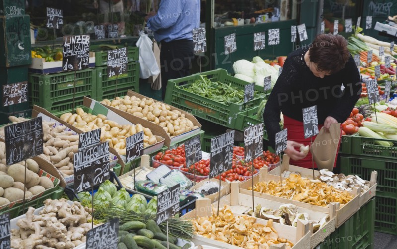 Vienna, Austria. The Naschmarkt. Stallholder selecting mushrooms from display of fresh produce also including potatoes ginger cucumbers and squash. Austria Austrian Republic Vienna Viennese Wien Europe European City Capital Naschmarkt Market Display Fresh Food Fruit Vegetables Veg Vegetable Stall Shop Store Destination Destinations Osterreich Viena Western Europe