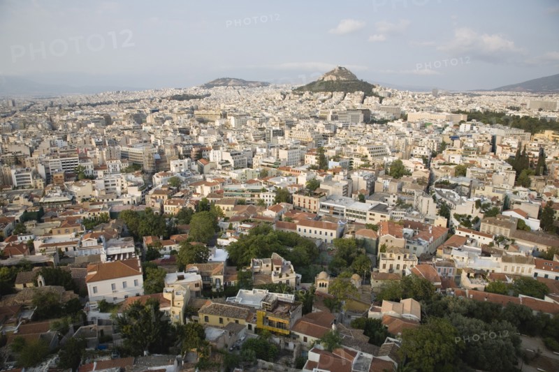 Athens, Attica, Greece. Mount Lycabettus rising in central Athens with densely populated city below part framed by wall in foreground. Greece Greek Europe European Vacation Holiday Holidays Travel Destination Tourism Ellas Hellenic Attica Athens City View Cityscape Aerial Elevated Houses Housing Mount Lycabettus Atenas Athenes Destination Destinations Ellada Southern Europe