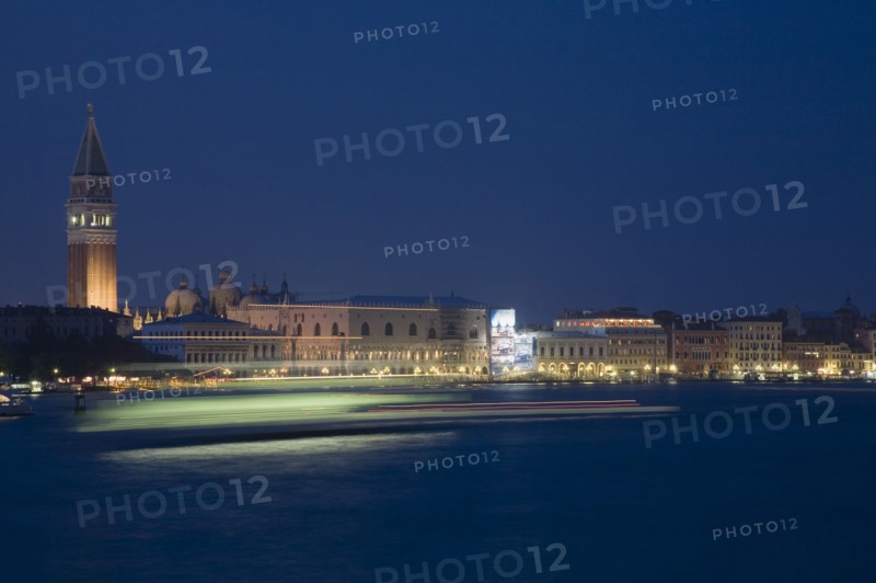 Venice, Veneto, Italy. Giudecca island Early evening view towards illuminated Campanile of St. Mark with vaporetto water bus to Murano and Burano in blurred motion in foreground with light trails reflected in water of the canal. Italy Italia Italian Venice Veneto Venezia Europe European City Illuminated Night Transport Transport Light Streaked Streaks Streak Movement Blurred Blur Bus Water Vaporetto Campanile St Saint Mark Marks Destination Destinations Nite Religion Southern Europe Warm Light
