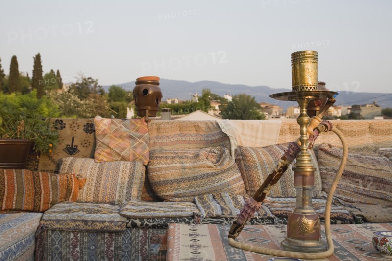 Selcuk, Izmir Province, Turkey. Ephesus. View from rooftop cafe with water pipe on table in foreground and traditional kilim textiles. Turkey Turkish Eurasia Eurasian Europe Asia Turkiye Izmir Province Selcuk Ephesus Cafe Rooftop Waterpipe Water Pipe Smoke Smoking Kilim Textiles Bar Bistro Classic Classical Cloth Destination Destinations European Historical History Historic Middle East Older Restaurant South Eastern Europe Western Asia