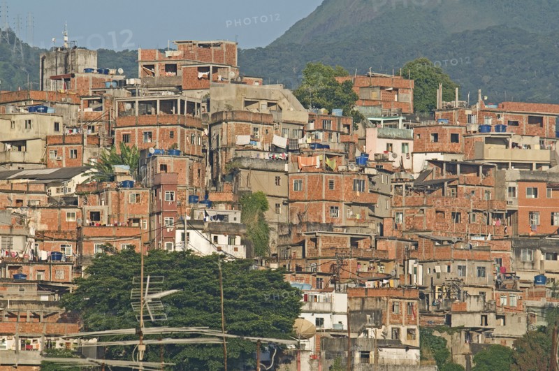 Rio de Janeiro, Brazil. Favela or slum on hillside above Copacabana neighbourhood bedcovers and washing hanging on lines unplastered red brick houses greenery and TV antenna. Brazil Brasil Brazilian Brasilian South America Latin Latino American City Urban Architecture Houses Housing Homes Copacabana Neighborhood Neighbourhood Favela Favelas Slum Slums Church Rio de Janeiro Aerial Clean Cleaning Destination Destinations Latin America Laundry Shanty South America Southern