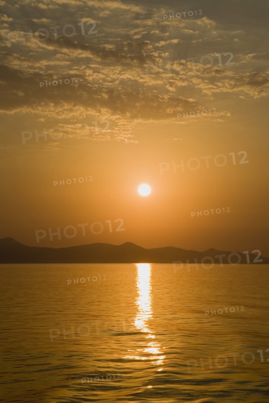 Samos, Northern Aegean, Greece. Vathy. Sunset over Samos seen from ferry between Samos and Athens as it leaves Vathy Samos with gold and orange sky reflected in water and silhouetted landscape. Greece Greek Europe European Vacation Holiday Holidays Travel Destination Tourism Ellas Hellenic Nortehrn Aegean Samos Island Vathy Sunet Sunt Orange Sky Sea Water Reflected Reflection Ripples Atenas Athenes Blue Color Destination Destinations Ellada Reflexion Scenic Solid Outline Shade Silhouette Southern Europe Sundown Atmospheric